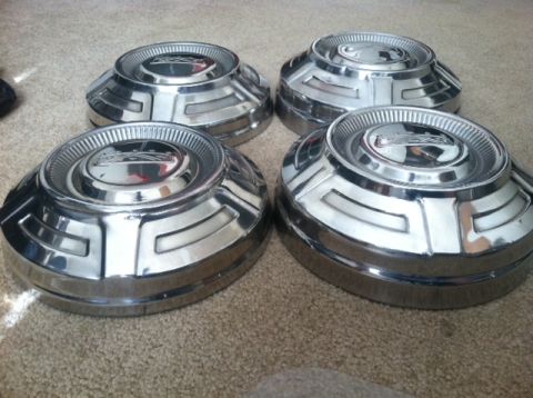 1977 Ford F-350 - Four chrome hubcaps are shown resting on a carpeted surface.