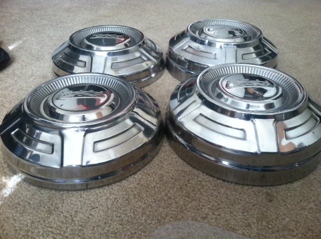 four chrome hubcaps on a carpeted floor