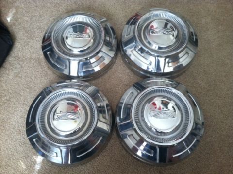 1977 Ford F-350 - Four chrome hubcaps are displayed on a carpeted surface, with a visible watermark at the bottom right.