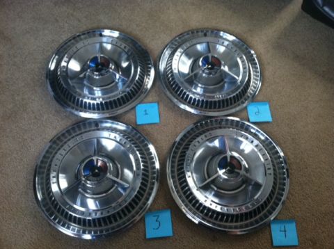 1965 Ford Thunderbird - Four vintage hubcaps are displayed on a carpeted surface, each with visible text around the center.