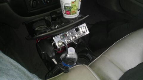 2000 Mercury Grand Marquis - A CB radio is mounted in the center console of a car, with a cup holder and a bottle of water nearby.