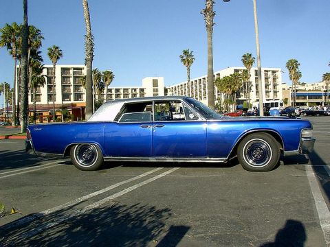 1991 Ford LTD Crown Victoria - A classic blue 1967 Lincoln Continental sedan with a silver roof is seen parked in a lot, with palm trees and buildings in the background.