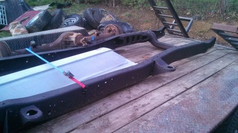 1979 Ford Bronco - The frame of a 1979 Ford Bronco is visible, strapped down on a trailer with other parts in the background.