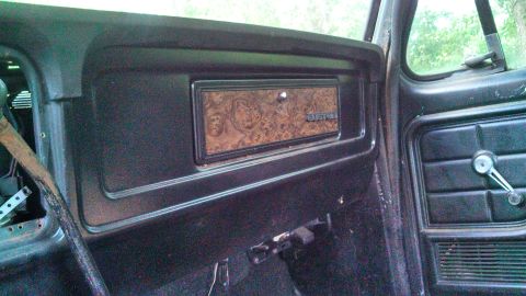1979 Ford Bronco - Passenger-side interior of an older Ford pickup showing a woodgrain glovebox panel, door panel and chrome window crank.