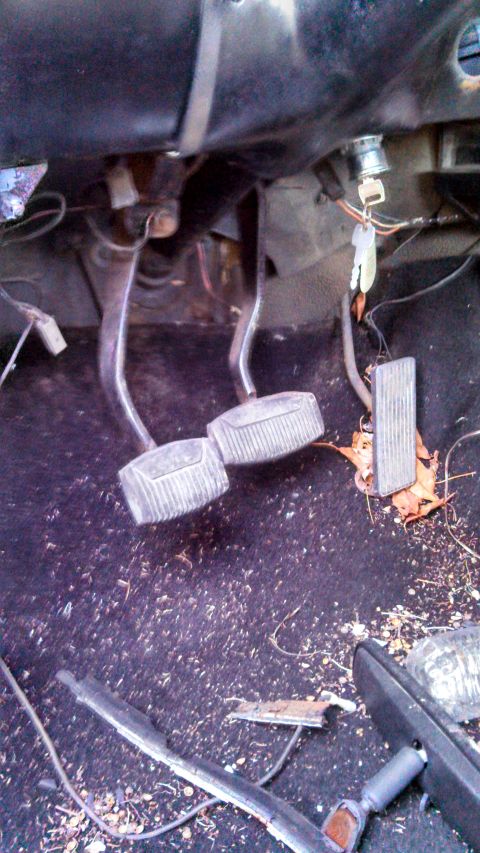 1979 Ford Bronco - The interior of a vehicle shows the brake and clutch pedals, ignition with keys, and debris on the floor.
