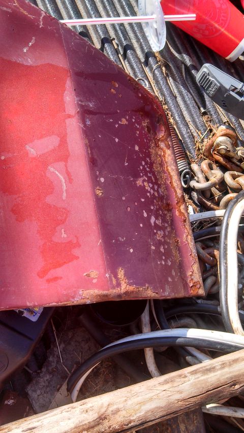 1979 Ford Bronco - A heavily rusted red car door is visible in the back of a truck, surrounded by other scrap metal and hoses.