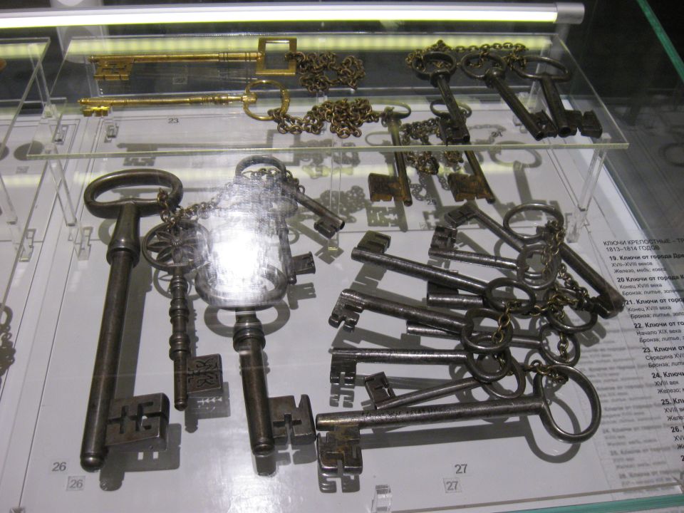 Collection of antique keys on display, some with chains, on glass shelves with labels
