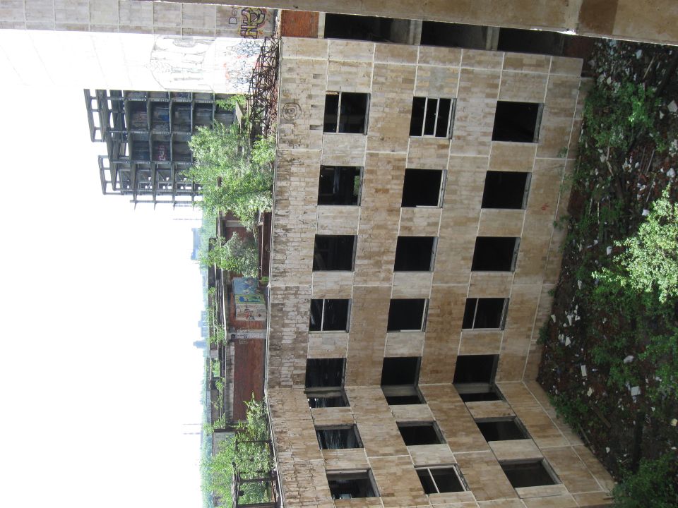 Dilapidated concrete building with many broken windows and overgrown vegetation