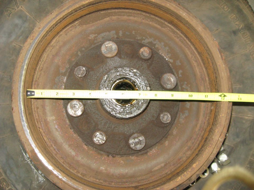Close-up of a rusty wheel hub with a brake drum and tire. A yellow measuring tape is across the hub
