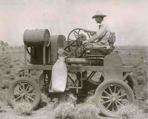 1909 Ford Model T - A man operates a vintage tractor in a field, with a large barrel mounted on the rear.
