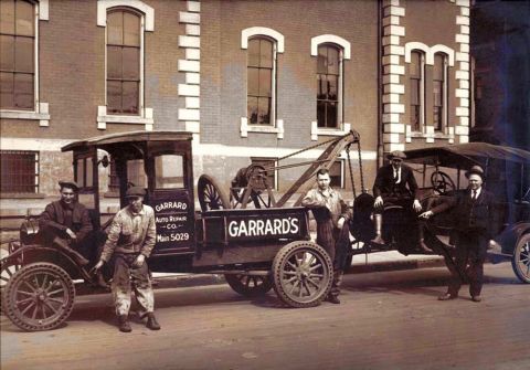 1909 Ford Model T - A tow truck with a crane is parked next to a car, with several men standing around them.