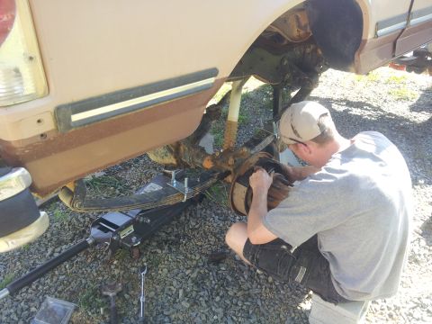 1988 Ford Bronco - A person is working on the rear suspension of a vehicle, possibly a Ford Bronco, with a jack supporting it.