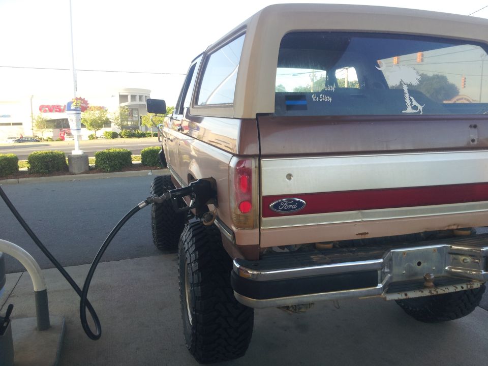 1988 Ford Bronco with large tires refueling at a gas station, rear view