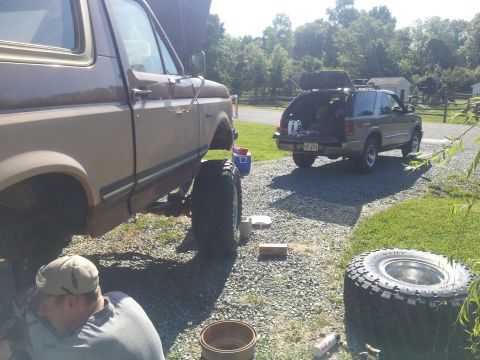 1988 Ford Bronco - Two SUVs are parked in a driveway, with one undergoing maintenance and its hood open.