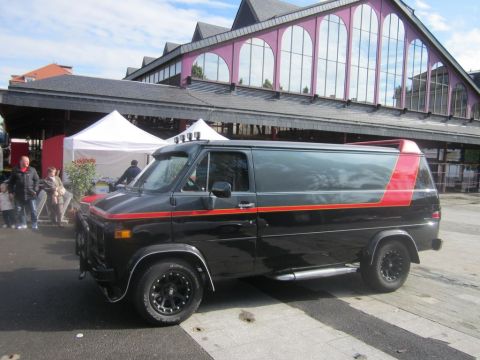 1991 Ford LTD Crown Victoria - This black van features a distinctive red stripe and a red accent on the rear, seen from the side.