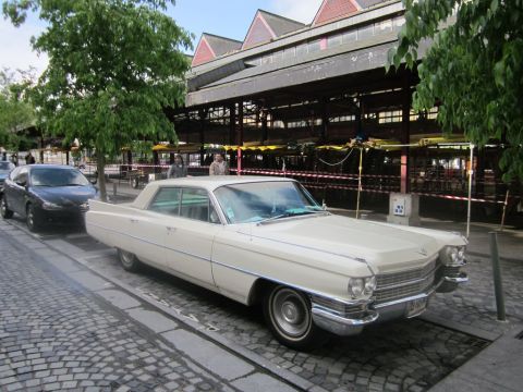 1991 Ford LTD Crown Victoria - A vintage Cadillac is parked on a street in front of a market building.