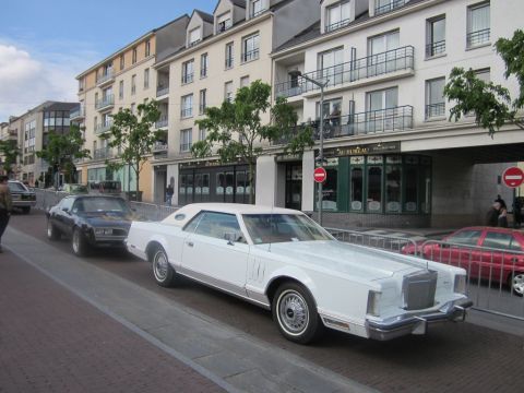 1991 Ford LTD Crown Victoria - A white 1980 Lincoln Continental Mark VI is parked on a street with other vehicles and buildings in the background.