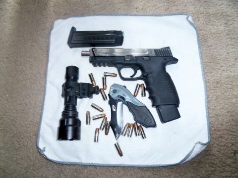 2000 Mercury Grand Marquis - A collection of firearm accessories including a pistol, magazine, ammunition, a folding knife, and a tactical flashlight are laid out on a…