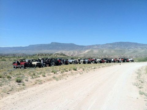 1987 Suzuki Samurai - A group of off-road vehicles are parked in a line on a dirt road under a clear blue sky.