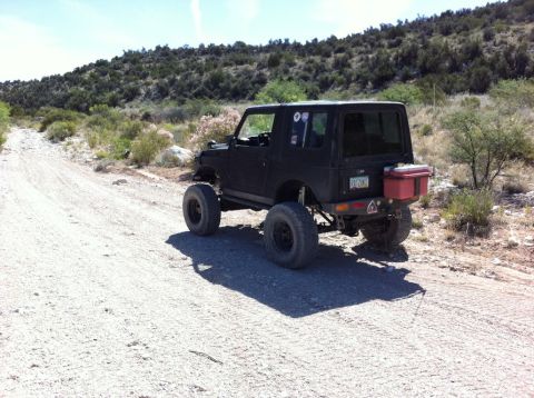 1987 Suzuki Samurai - A modified 1987 Suzuki Samurai is parked on a dusty, rural road with scrub brush and hills in the background.