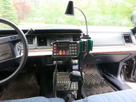 1991 Ford LTD Crown Victoria - car interior showing the steering wheel, dash, and a center-mounted two-way radio with keypad and handheld mic.