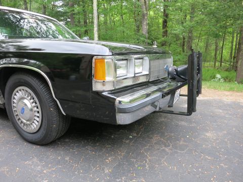 1991 Ford LTD Crown Victoria - Front corner of a black sedan equipped with a heavy steel push bumper, stacked headlights, and amber turn signal.