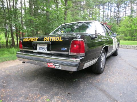 1991 Ford LTD Crown Victoria - Rear three-quarter view of a black Ford sedan with gold Highway Patrol trunk lettering and a California 888849 plate.