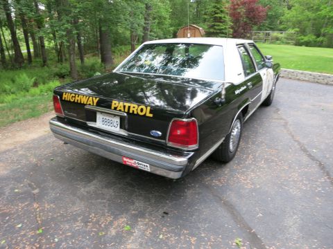 1991 Ford LTD Crown Victoria - Black police sedan photographed from the rear three-quarter, gold Highway Patrol trunk lettering above a Ford emblem and plate.