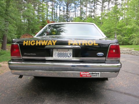 1991 Ford LTD Crown Victoria - Rear of a black Ford Crown Victoria police car showing gold Highway Patrol lettering, California plate, and twin tail lights.
