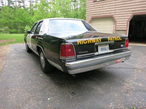 1991 Ford LTD Crown Victoria - Black Ford Crown Victoria cruiser shown from the rear quarter near a shingled garage, with gold Highway Patrol trunk lettering.