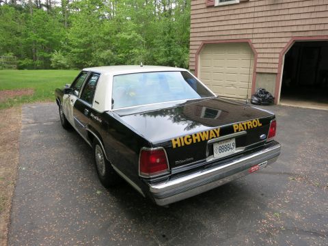 1991 Ford LTD Crown Victoria - Black Ford Crown Victoria police sedan viewed from rear three-quarter in a paved driveway beside a house garage.