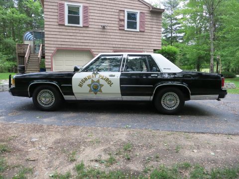 1991 Ford LTD Crown Victoria - Driver-side profile of a black-and-white Highway Patrol sedan fitted with a front push bar, parked in a driveway.