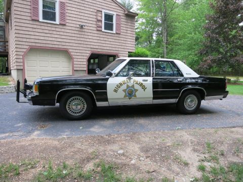 1991 Ford LTD Crown Victoria - Side-profile view of a black-and-white Highway Patrol sedan with front push bumper and door star, parked before a garage.