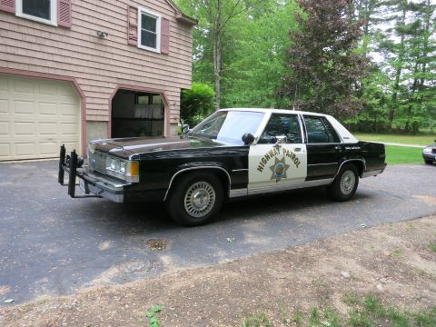 1991 Ford LTD Crown Victoria - Black-and-white Highway Patrol sedan shown from front driver quarter with a steel push bar, parked in a driveway.