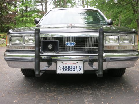 1991 Ford LTD Crown Victoria - Close front view of a black Ford sedan showing Ford-emblem grille, steel push bar, and a California 888849 license plate.
