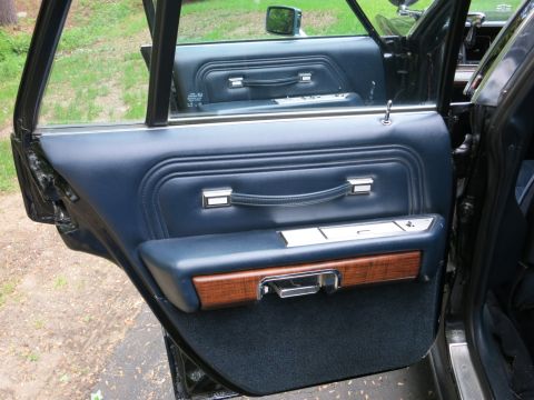 1991 Ford LTD Crown Victoria - Interior of an open rear car door with navy padded panel, chrome grab handle, woodgrain trim and dark carpet.