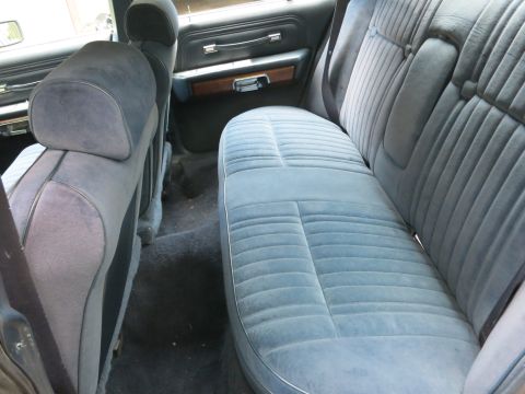 1991 Ford LTD Crown Victoria - Blue cloth velour rear bench seat inside a sedan, viewed through the open door with a folded seat back at left.