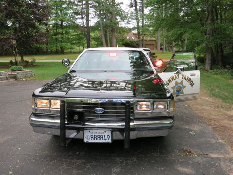 1991 Ford LTD Crown Victoria - Black-and-white Ford sedan styled as a Highway Patrol car, push bar and roof light, parked in a wooded driveway.