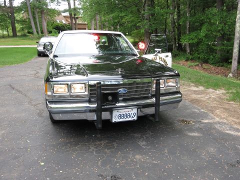 1991 Ford LTD Crown Victoria - Front angled view of a black Ford sedan with push bumper and California plate 888849, another car parked behind it.