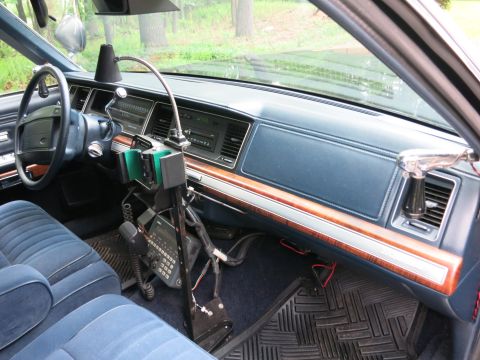 1991 Ford LTD Crown Victoria - View across a sedan dashboard with woodgrain trim, blue interior and a floor-mounted radio/console stand at center.