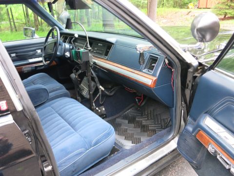 1991 Ford LTD Crown Victoria - Interior of a sedan seen through the open passenger door, with blue cloth seats, woodgrain dash and a center radio stand.