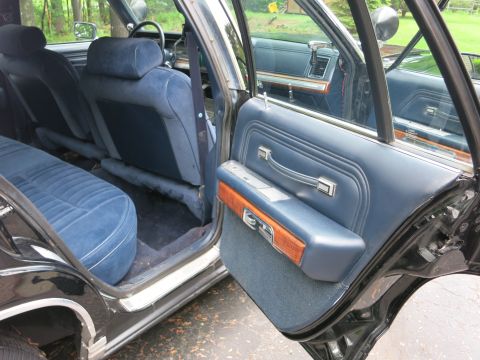 1991 Ford LTD Crown Victoria - Open rear door of a black sedan revealing blue cloth rear seating and a navy door panel with woodgrain accent.