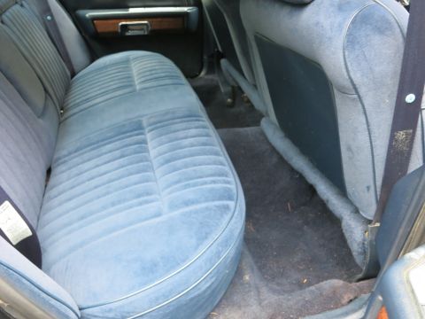 1991 Ford LTD Crown Victoria - Rear passenger area of a sedan showing a blue cloth bench seat, dark carpet and the driveline hump.