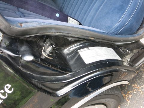 1991 Ford LTD Crown Victoria - Close-up of a black car's lower door jamb and rocker with a white printed information label near the blue seat edge.