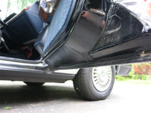 1991 Ford LTD Crown Victoria - Low-angle view of a black car's open door and rocker panel with a styled steel wheel on the ground beyond.