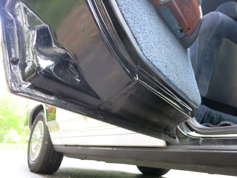 1991 Ford LTD Crown Victoria - Low-angle view of a black car's open door, lower body and chrome rocker, with blue cloth interior beyond.