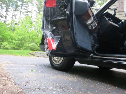 1991 Ford LTD Crown Victoria - Low-angle view of a black sedan with the rear door open, revealing a dented quarter panel marked with red tape.