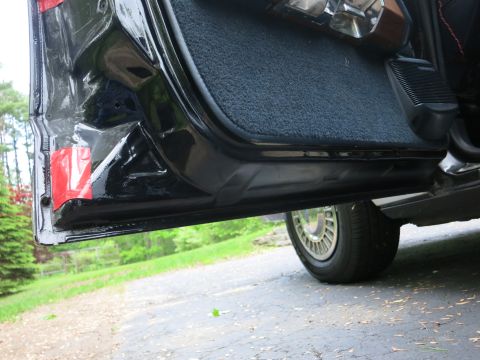 1991 Ford LTD Crown Victoria - Close-up of an open black car's lower door edge and rocker panel, with a gold turbine-style wheel visible behind on a paved driveway.