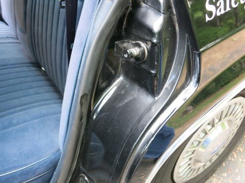 1991 Ford LTD Crown Victoria - View along a black car's door pillar and hinge with blue cloth seating inside and a gold spoked wheel behind.