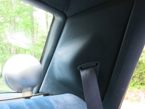 1991 Ford LTD Crown Victoria - Rear interior corner of a car with a silver spherical light, dark headliner, seatbelt and blue cloth seat.